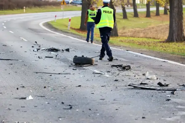 Na drodze po kolizji leżą szczątki, opona i inne elementy. Policjanci w kamizelkach odblaskowych badają miejsce zdarzenia, być może szukając śladów ucieczki z miejsca kolizji.