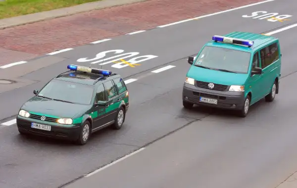 Dwa pojazdy uprzywilejowane Straży Granicznej na drodze. Jeden to ciemnozielony Volkswagen Passat kombi, drugi to turkusowy Volkswagen Transporter.