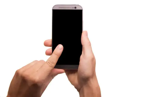 Dłoń trzymająca smartfon z czarnym ekranem, palec wskazujący dotyka ekranu.