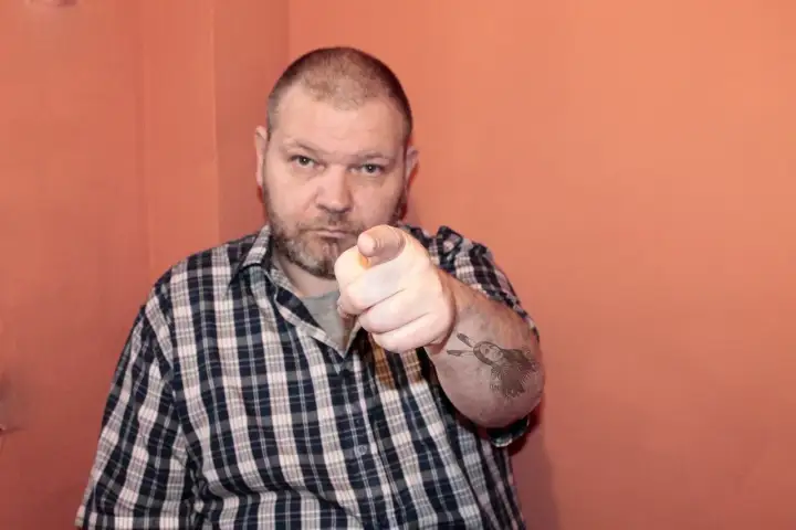 Mężczyzna w kratę wskazuje palcem, na ramieniu tatuaż z Indianinem. "234 kk" - czy to jego numer?